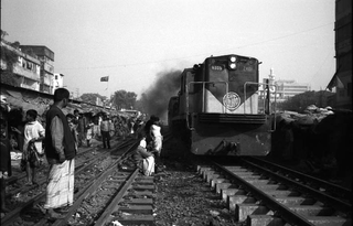 Bangladesh, 103-045-29
Persone sui binari della ferrovia guardano il passaggio di un treno, 2009
Dacca (Kawran Bazar) (Bangladesh)